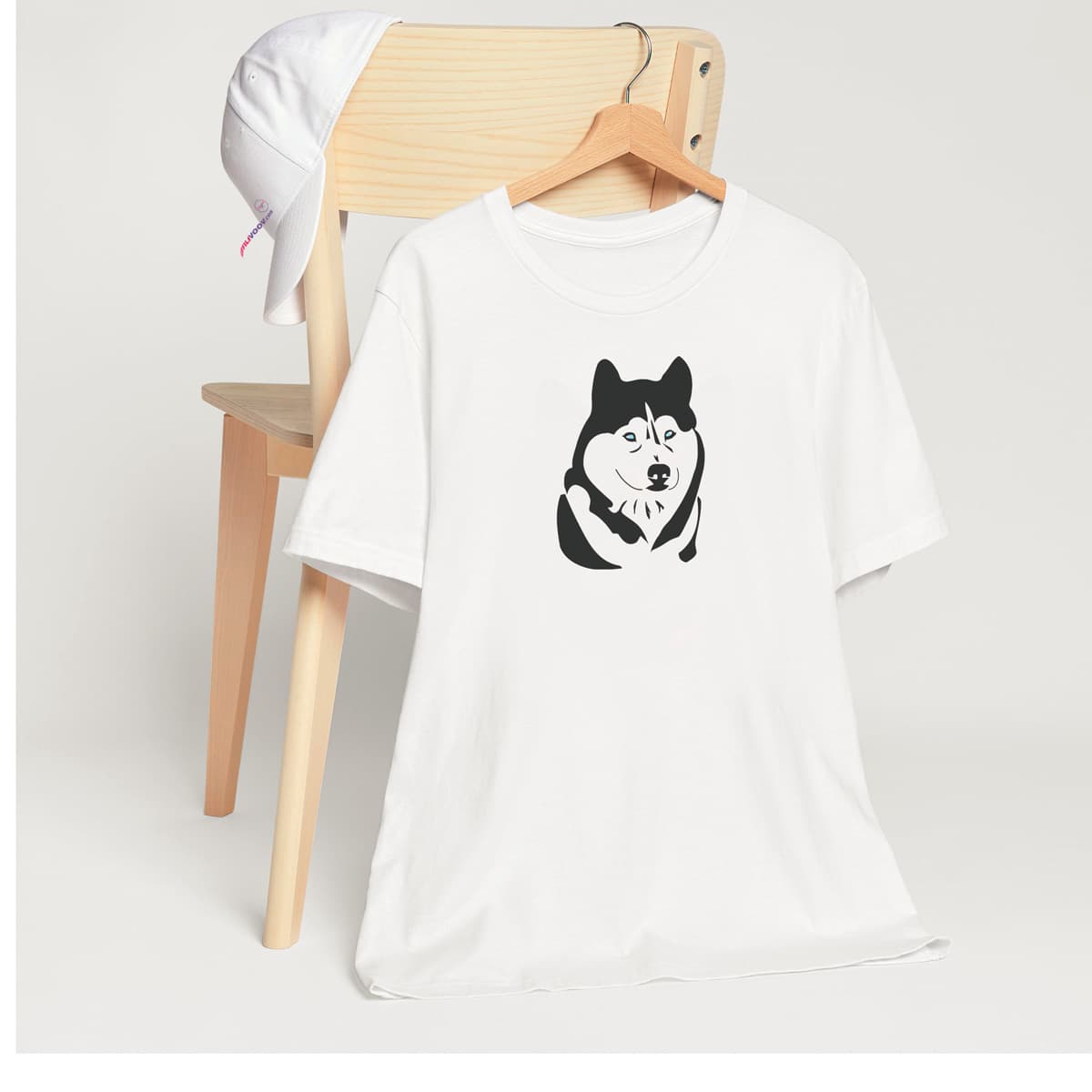 White crew neck short sleeved t-shirt, features a one-line graphic silhouette of a cute hand-drawn Husky's face with sparkling blue eyes.T-shirt hanging on chair shown in close-up to highlight print and size.