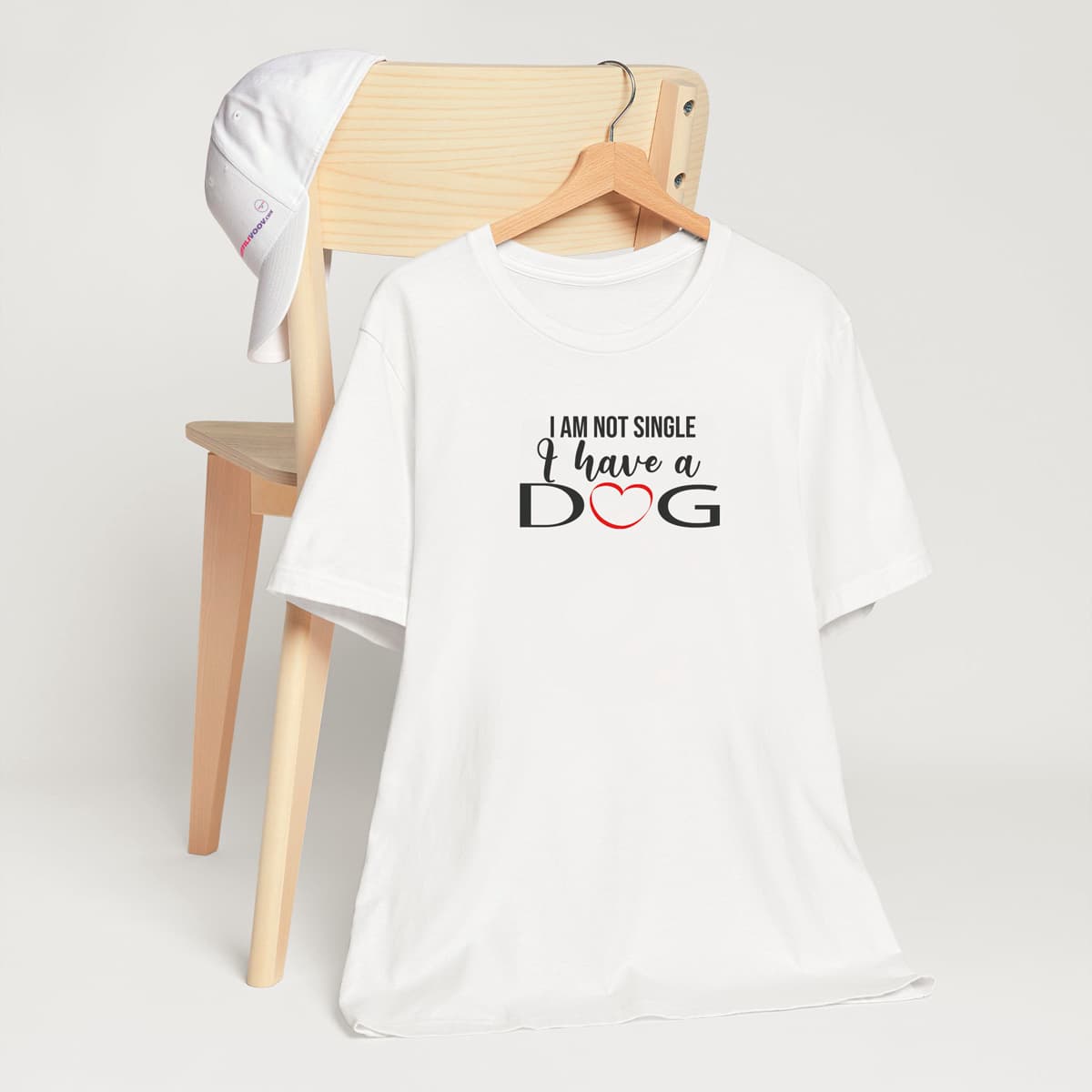 White crew neck short sleeved t-shirt. Showcases with humor a text saying "I am not single I have a dog". T-shirt hanging on chair shown in close-up to highlight print and size