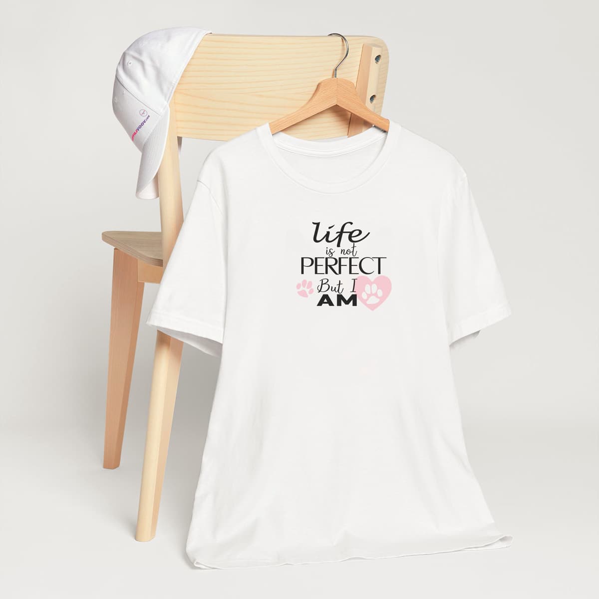 White crew neck short sleeved t-shirt, feature a fun statement, quote with a twist ”life is not perfect but I am”. T-shirt hanging on chair shown in close-up to highlight print and size