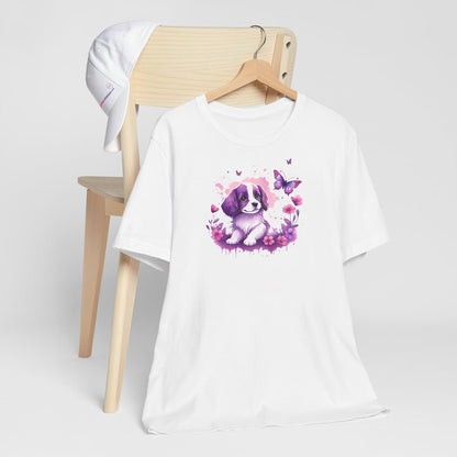 White crew neck short sleeved t-shirt, feature an Spaniel puppy, the epitome of adorable, frolicking amidst a kaleidoscope of blooms in a charming wicker basket. T-shirt hanging on chair shown in close-up to highlight print and size