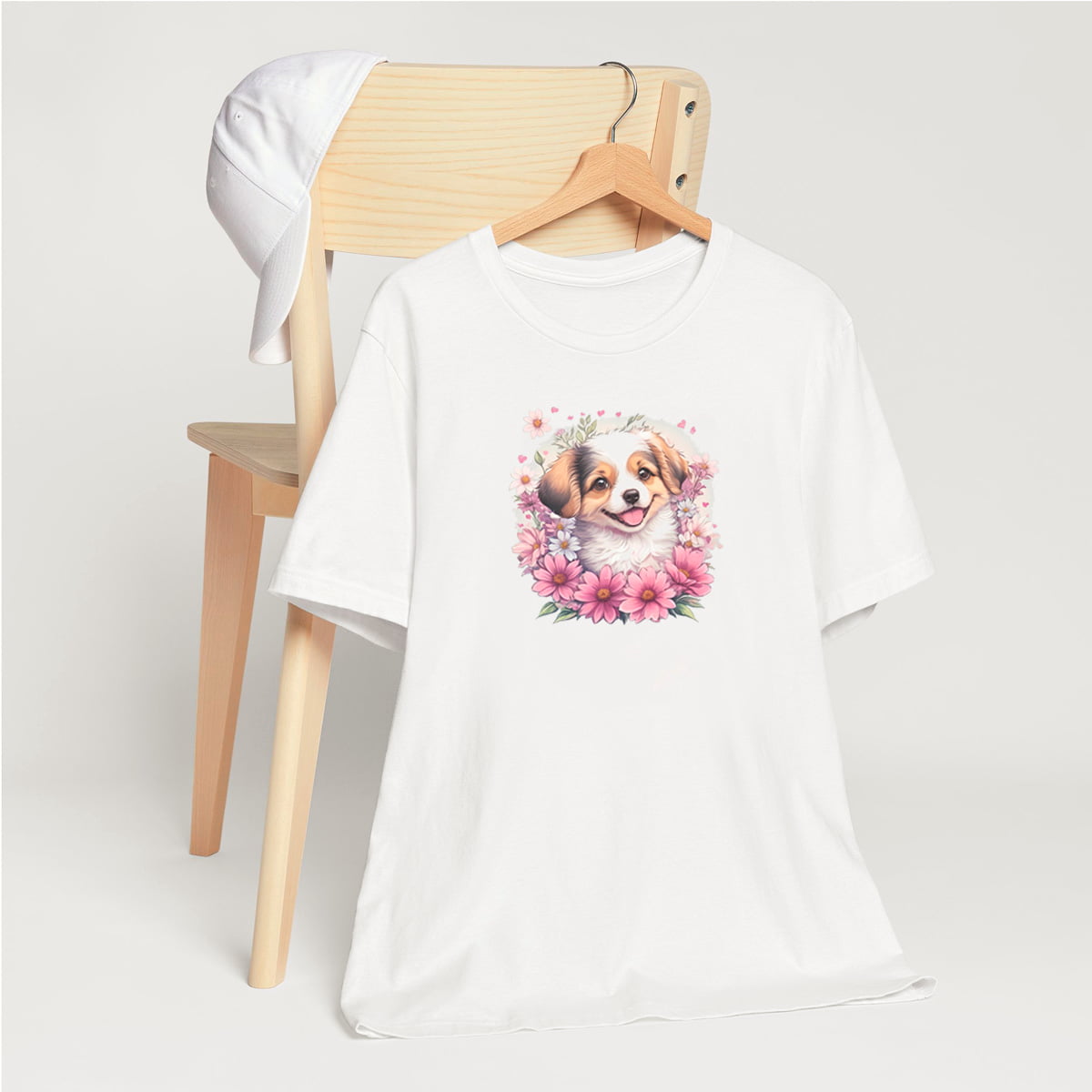White crew neck short sleeved t-shirt, stars a cheeky Aussie Shepherd pup amidst a whimsical wicker-basket garden. T-shirt hanging on chair shown in close-up to highlight print and size