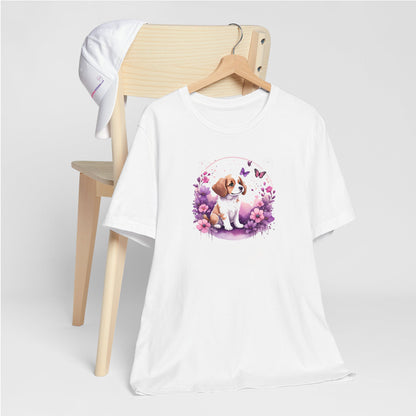 White crew neck short sleeved t-shirt, feature a playful pup amidst a whimsical floral fiesta. T-shirt hanging on chair shown in close-up to highlight print and size