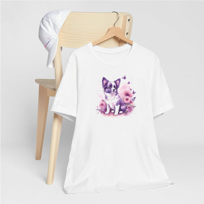White crew neck short sleeved t-shirt, features an adorable, lively puppy amidst a vibrant wicker basket brimming with floral splendor and playful butterflies. T-shirt hanging on chair shown in close-up to highlight print and size