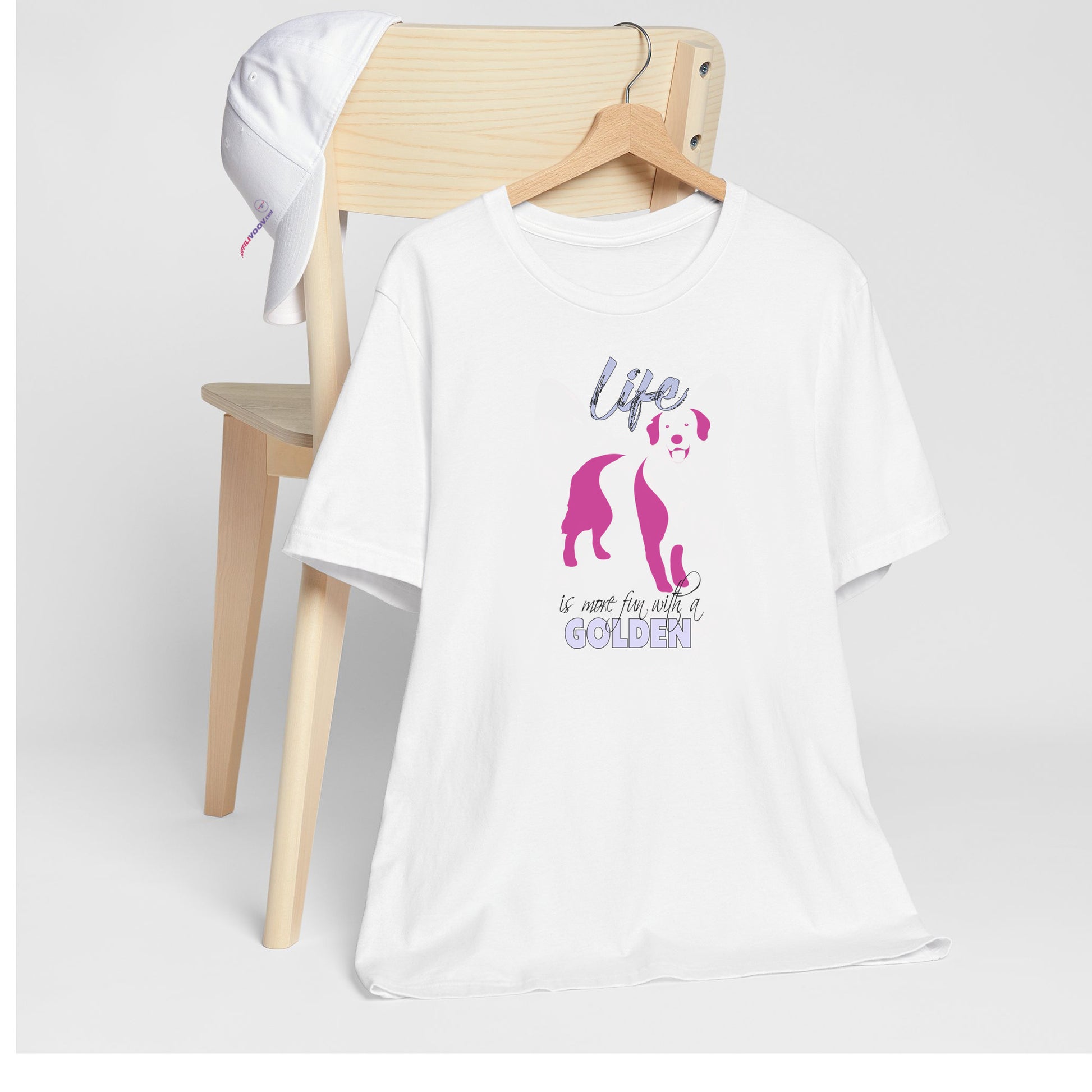 White crew neck short sleeved t-shirt. Featuring an adorable Golden Retriever silhouette in cute pink, the tee also boasts a bold "Life" message and empowering "is more fun with a Golden" phrase. T-shirt hanging on chair shown in close-up to highlight print and size.
