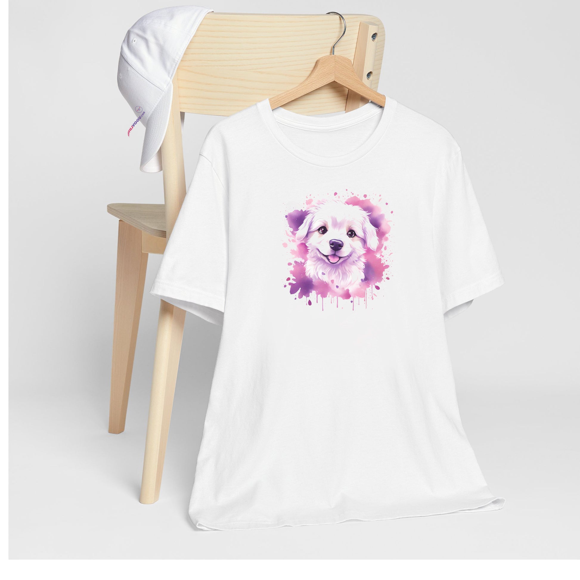 White crew neck short sleeved t-shirt. Featuring an enchanting Maltese puppy amidst a tapestry of splash artistry in vibrant pink and purple toned colors. T-shirt hanging on chair shown in close-up to highlight print and size