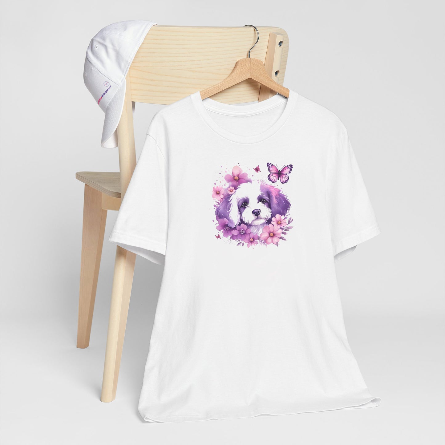 White crew neck short sleeved t-shirt, feature a cute Maltese puppy face, in nestle butterflies and floral garden. T-shirt hanging on chair shown in close-up to highlight print and size