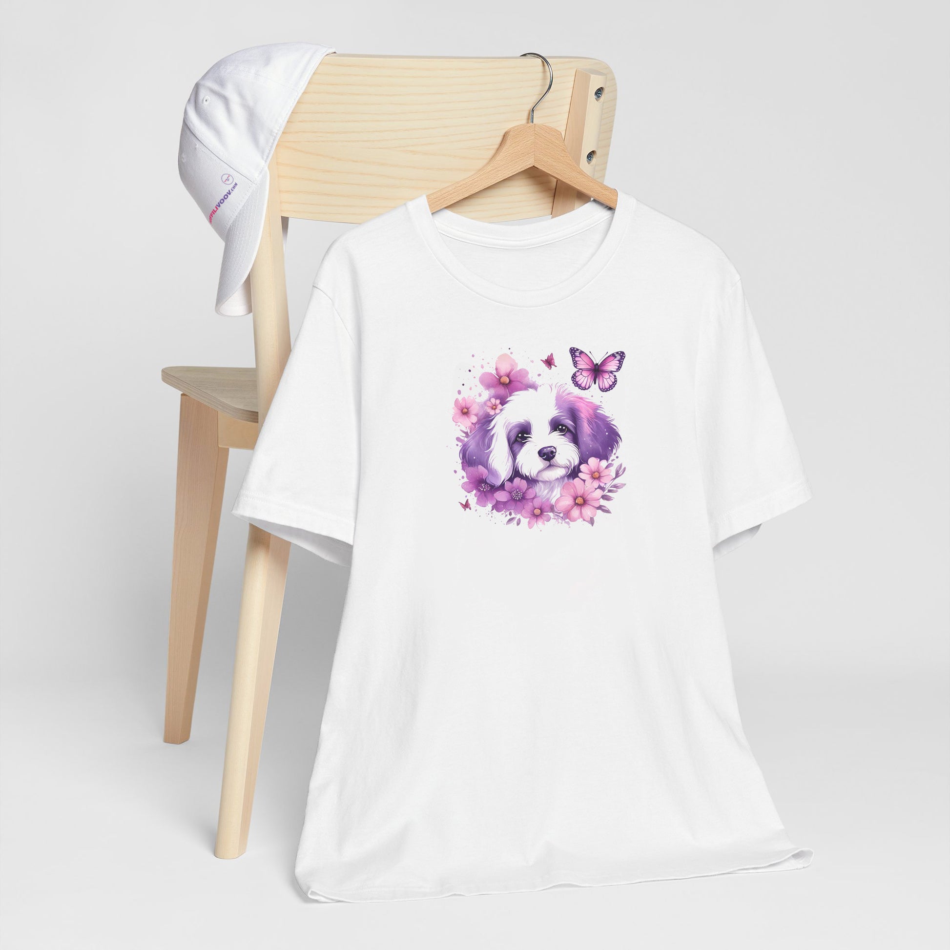 White crew neck short sleeved t-shirt, feature a cute Maltese puppy face, in nestle butterflies and floral garden. T-shirt hanging on chair shown in close-up to highlight print and size