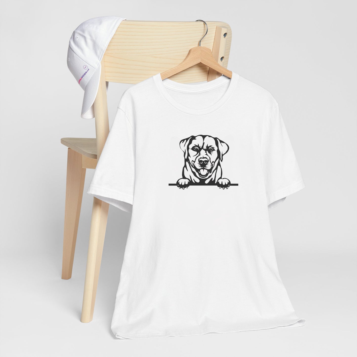 White crew neck short sleeved t-shirt. Features a cute black and white hand-drawn graphic of a Labrador dog with paws on the table. T-shirt hanging on chair shown in close-up to highlight print and size.