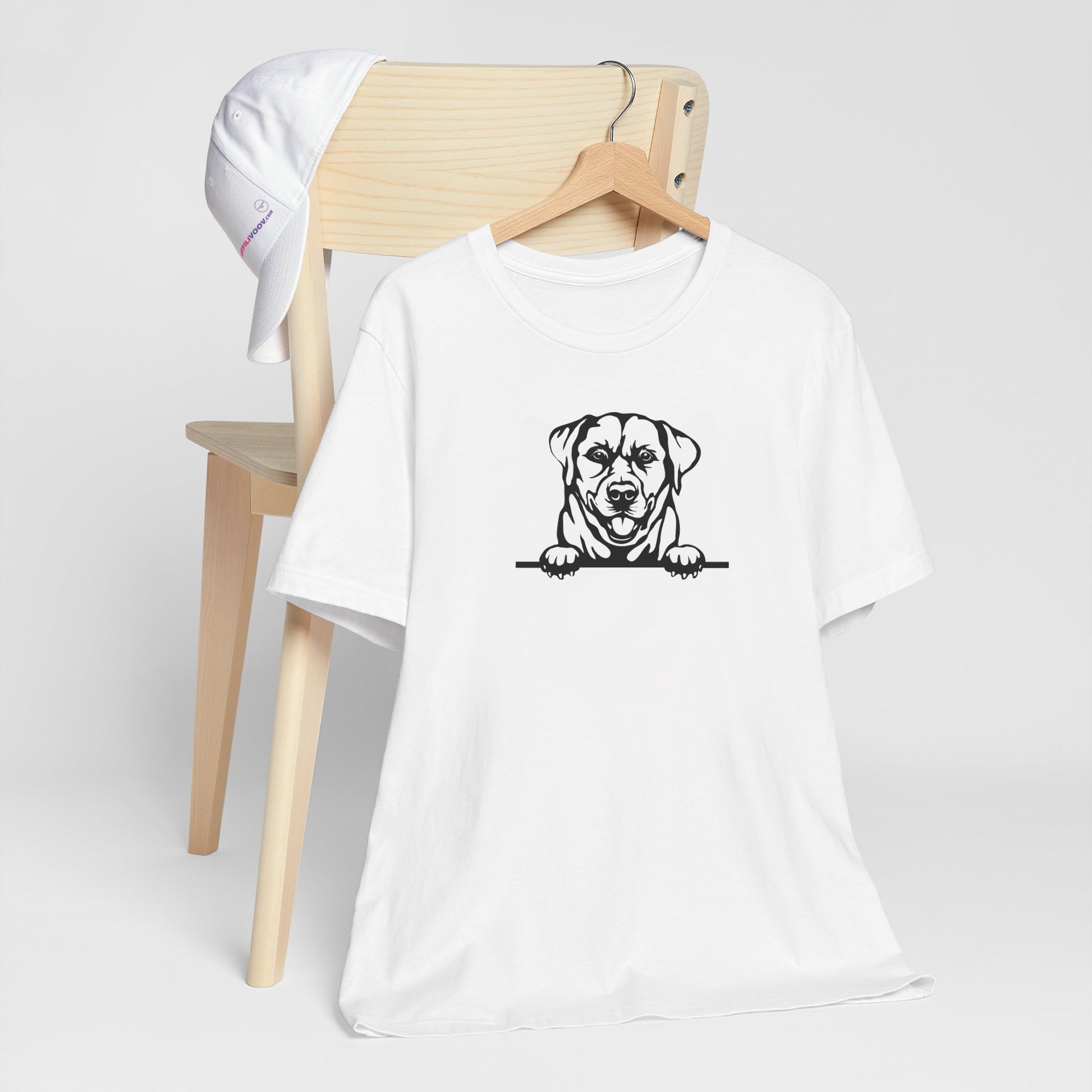 White crew neck short sleeved t-shirt. Features a cute black and white hand-drawn graphic of a Labrador dog with paws on the table. T-shirt hanging on chair shown in close-up to highlight print and size.