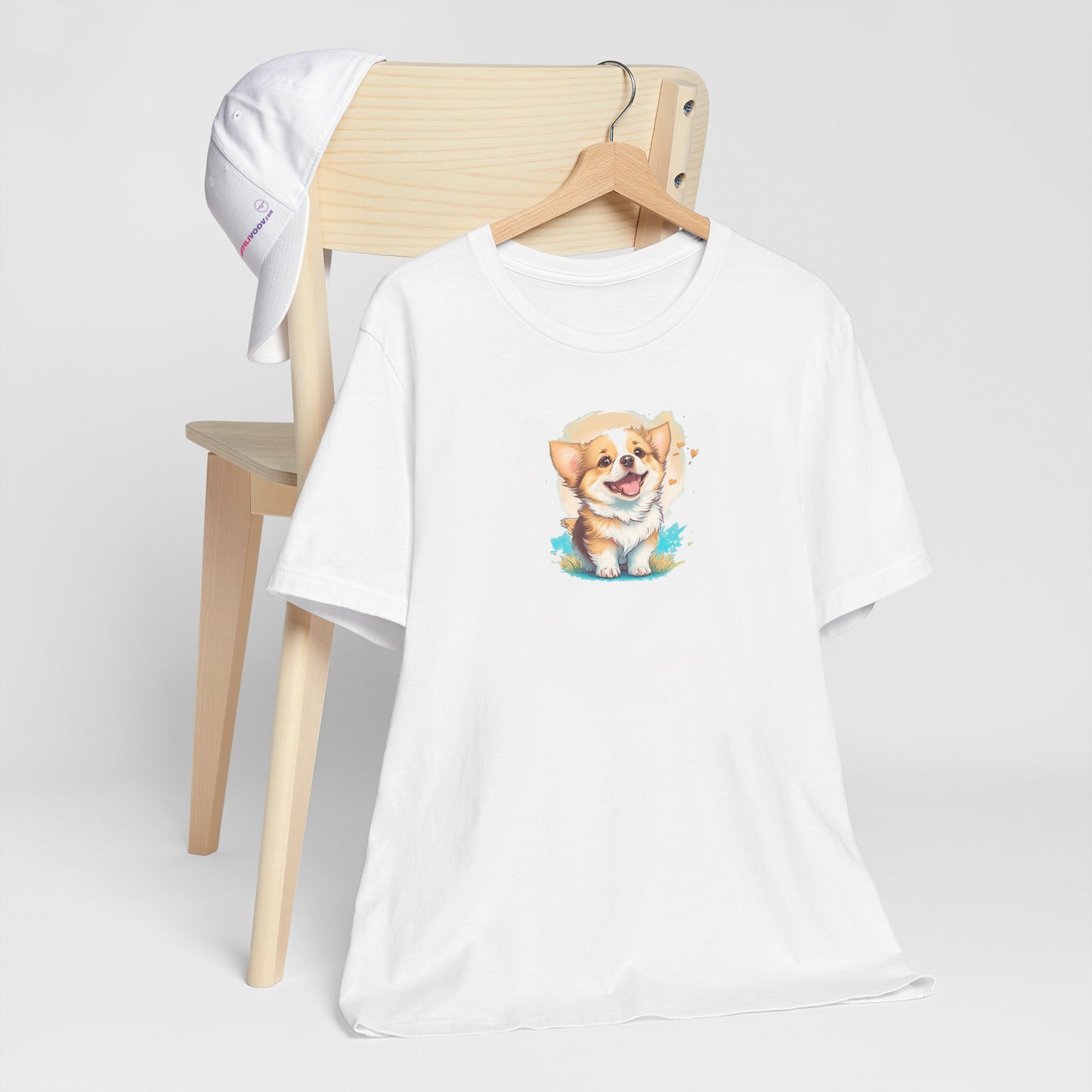 White crew neck short sleeved t-shirt, an adorable, happy Welsh Corgi puppy at the heart of a whimsical world of flowers and hearts. T-shirt hanging on chair shown in close-up to highlight print and size.