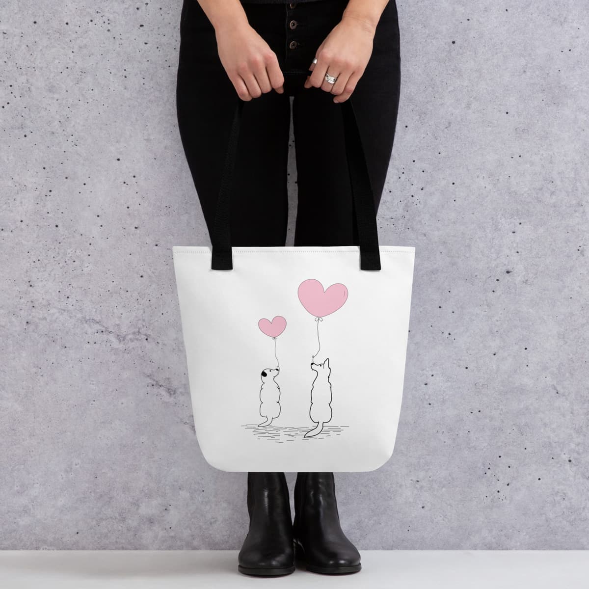 Model showcase a Uni-size 15"x15" white tote polyester canvas bag, with black stripped handle, featuring a charming graphic of two adorable dogs sitting together and holding onto pink balloons.