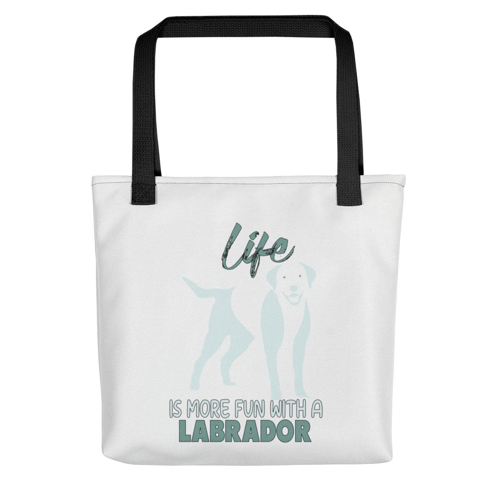 White spun canvas fabric tote bag , on the bag is a black one-line graphic print silhouette of a cute Labrador dog standing with its tongue out. Above the dog is the text " LIFE" in cap and underneath the dog is the text " is more fun with a Labrador " in cap" 