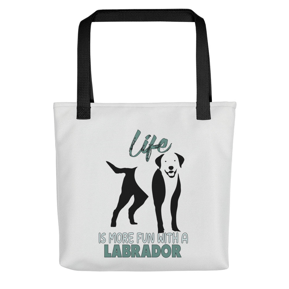 White spun canvas fabric tote bag , on the bag is a black one-line graphic print silhouette of a cute Labrador dog standing with its tongue out. Above the dog is the text " LIFE" in cap and underneath the dog is the text " is more fun with a Labrador " in cap" 