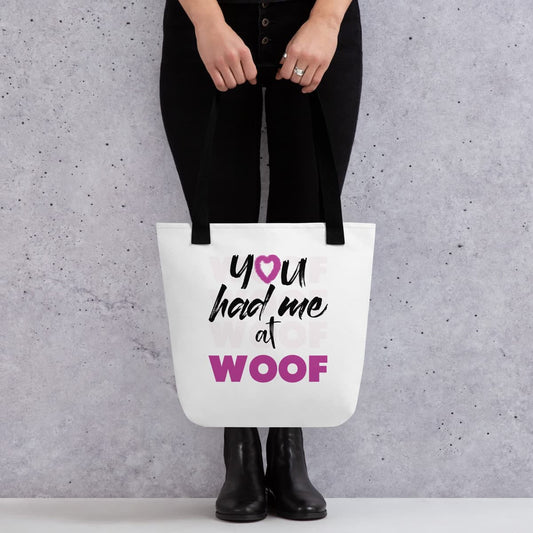 Uni-sizes 15"x15" white tote canvas bag, with black stripped handle, feature a classic quote you had me at woof, the letter o, is a pink colored fluffy heart same with the text ”woof” which is underlay and repeated several times. Printed front and back. Female model shown in close-up to highlight print and fit.