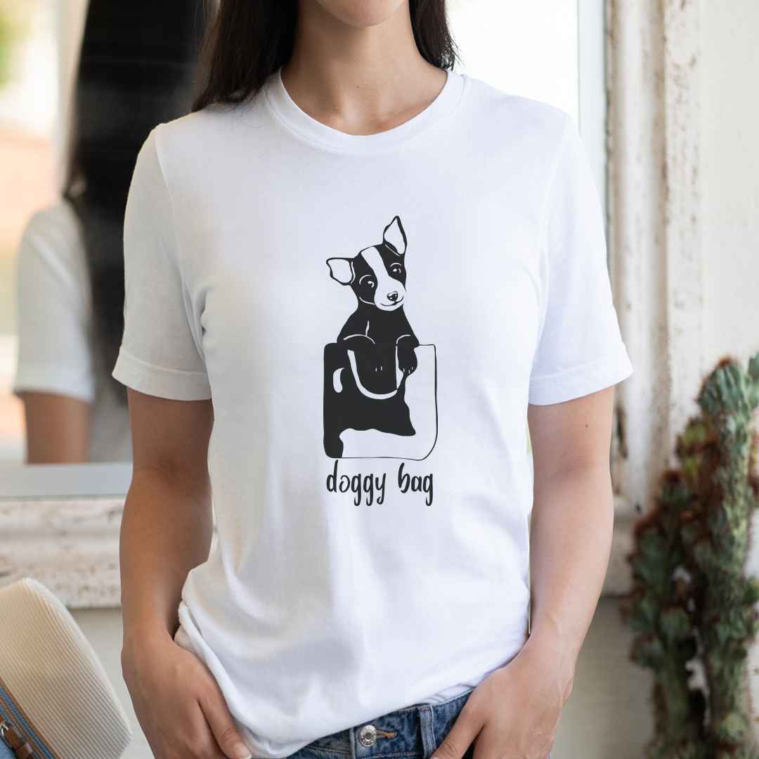 cotton crew neck shirt, short sleeved, on the apparel is a graphic print with a cute puppy face,sticking its head up of a bag, below the bag is the text "Doggy Bag"