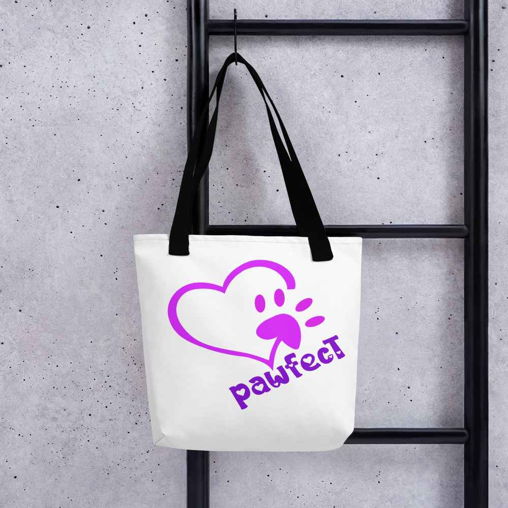 Hanging on a hook a White spun canvas fabric tote bag, with black handle stripped, on the tote is  cute graphic pink shaped heart with a paw on the side, underneath the heart is the tilted text "pawfect"  in color purple
