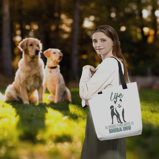 Young dog lover women, standing in a a park carry on her shoulder a white tote polyester canvas bag, with black stripped handle, feature a black one-line Shiba Inu print with life quote ”life is more fun with a Shiba Inu”. Printed front and back.