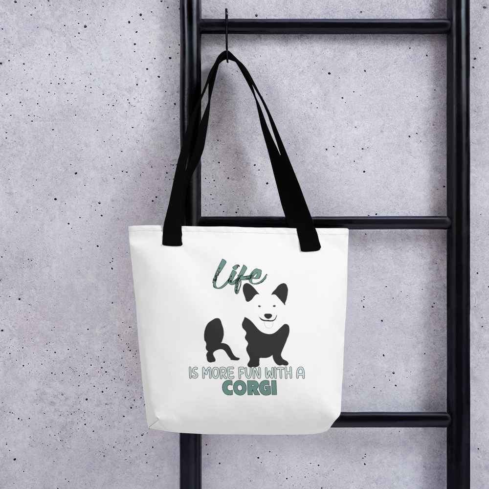 White spun canvas fabric tote bag , on the bag is a black one-line graphic print silhouette of a cute Welsh Corgi dog standing with its tongue out. Above the dog is the text " LIFE" in cap and underneath the dog is the text " is more fun with a Corgi " in cap" 