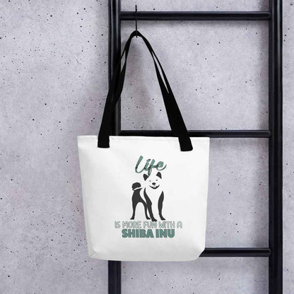 White spun canvas fabric tote bag , on the bag is a black one-line graphic print silhouette of a cute Shiba Inu standing with its tongue out. Above the dog is the text " LIFE" in cap and underneath the dog is the text " is more fun with a Shiba Inu " in cap