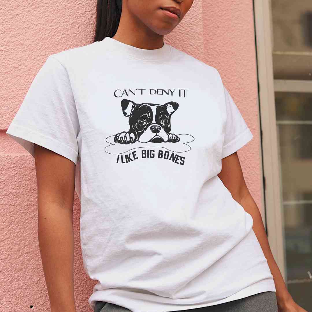 White cotton crew neck unisex  short sleeve tshirt, on the apparel is a black /white graphic bulldog face of a pop protecting it big dog bone, above the is the text "can´t deny it" below the dog bone is the text " i like big bones".