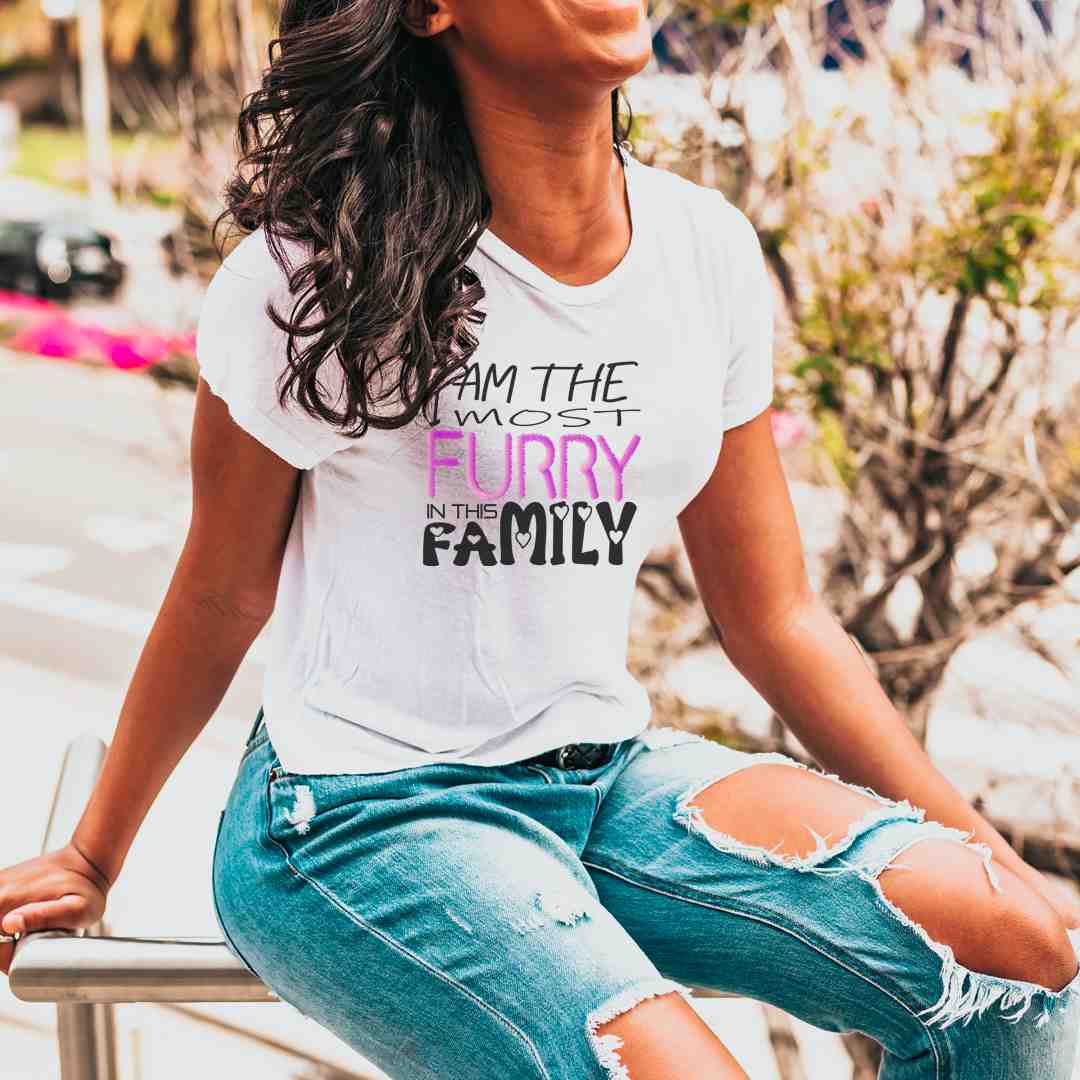 White cotton crew neck unisex  short sleeve tshirt, on the apparel is a graphic text saying " i am the most furry in this family" the text "furry" is with fluffy pink graphic. and the text "family" got small hearts in each of the letters.