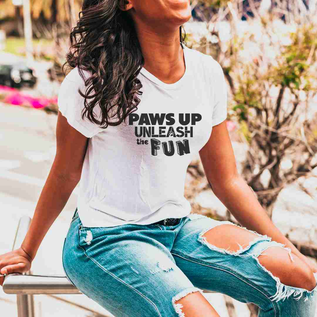 White cotton crew neck unisex  short sleeve tshirt, on the apparel is  a graphic text saying "paws up unleash the fun"